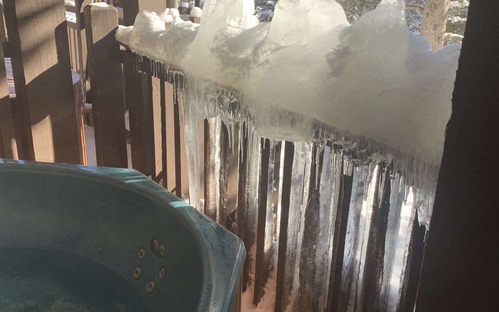 Thick ice and icicles on a deck railing beside a hot tub in Summit County